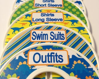 May include: Six colorful, round, plastic closet hanger dividers with dinosaur patterns. Each divider has a white label with a different clothing category: Pants, Shorts, Shirts Short Sleeve, Shirts Long Sleeve, Swim Suits, Outfits.