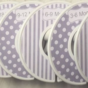 May include: A set of six white and lavender closet dividers for baby clothes. Each divider is circular with a white border and features a different age range label, including "0-3 Months" and "18-24". Some dividers have polka dots, others stripes.