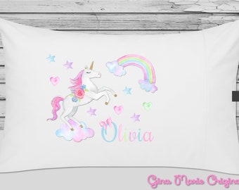 May include: White pillowcase with a watercolor illustration of a unicorn jumping over a rainbow. The unicorn is pink and white with a floral crown. The rainbow is multi-colored with clouds. The pillowcase also has stars, hearts, and the name "Olivia" written in pink and blue.