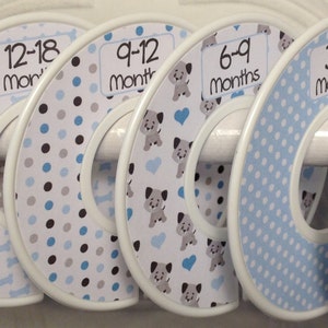May include: Six white plastic hangers with different coloured and patterned fabric circles. The circles are labelled with age ranges in months: 0-3, 3-6, 6-9, 9-12, 12-18, and 18-24 months.