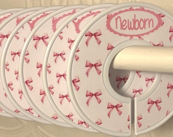 May include: Set of eight white plastic hanger dividers with pink bows and the word "newborn" printed on one divider.