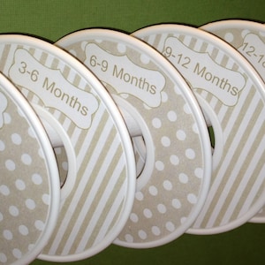 Puede incluir: Conjunto de seis separadores de perchas de plástico blanco con patrones de lunares y rayas marrones y blancos. Cada separador está etiquetado con un rango de edad diferente para la ropa de bebé: 0-3 meses, 3-6 meses, 6-9 meses, 9-12 meses, 12-18 meses y 18-24 meses.
