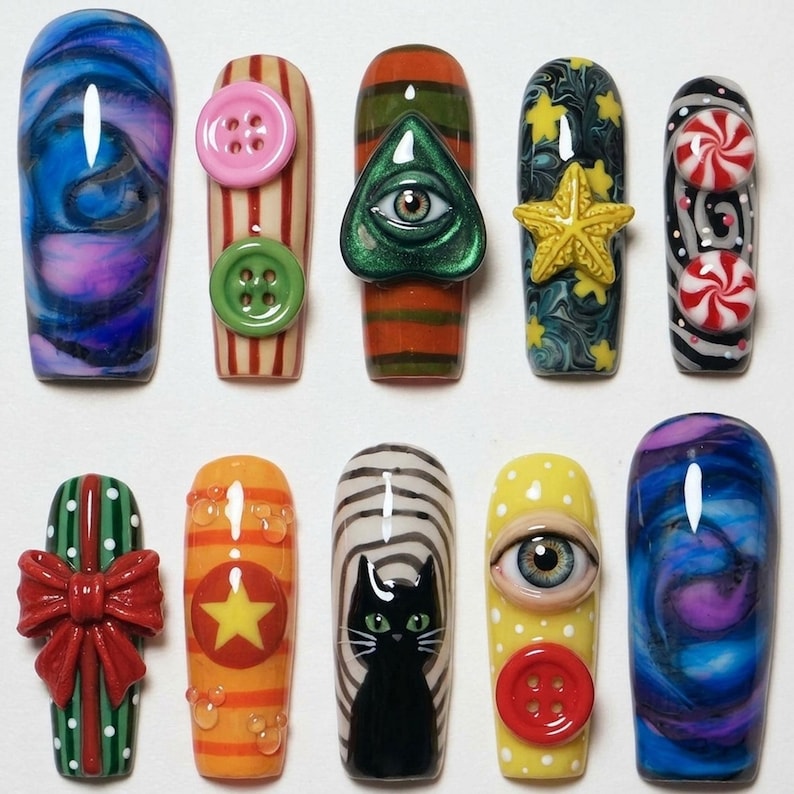 Puede incluir: Un conjunto de diez u&ntilde;as postizas con dise&ntilde;os variados que incluyen un patr&oacute;n de m&aacute;rmol azul y morado, u&ntilde;as a rayas con botones, un dije de ojo verde, una estrella amarilla, caramelos de menta rojos y blancos, un lazo rojo y un gato negro.
