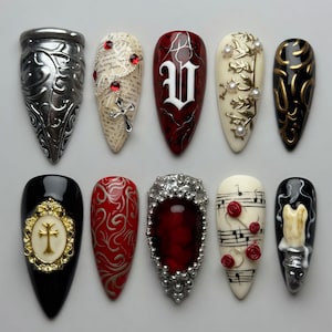 May include: A set of ten almond-shaped press-on nails featuring diverse designs including metallic silver filigree, script text with a cross charm, a red nail with a white letter V, cream nails with pearls or musical notes, and black nails with gold accents.