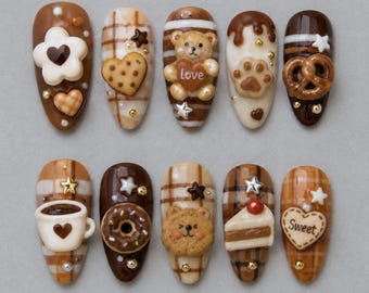 May include: A set of ten press-on nails featuring brown, cream, and white color palettes with 3D embellishments including a teddy bear holding a heart with the text Love, a coffee cup, a donut, a slice of cake, a pretzel, and a heart with the text Sweet.