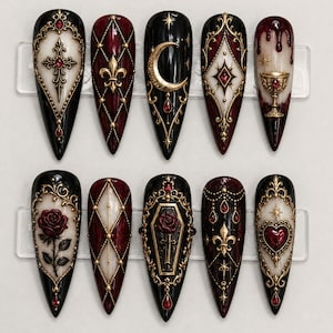 May include: A set of ten stiletto-shaped press-on nails featuring a black, white, and deep red color palette. The designs include gold filigree, a cross, a fleur-de-lis, a crescent moon, a chalice, a rose, a coffin, and a heart with red gems.