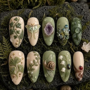 May include: A set of ten almond-shaped press-on nails featuring 3D nature-inspired designs. Decorations include ivy vines, a moth, a purple geode, mushrooms, moss, ginkgo leaves, a snail, lily of the valley, a beetle, and a ladybug with water droplets.