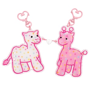 May include: Two acrylic keychains featuring a white camel and a pink giraffe, both decorated with colorful polka dots and pink outlines. Each keychain has a pink heart-shaped clasp, and the two figures are connected by a small white heart magnet.