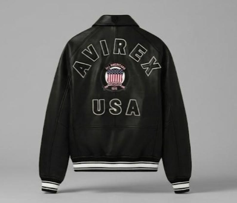 May include: A black leather varsity jacket featuring the text AVIREX in an arched white outline font across the upper back. Below is a circular patch with an American flag graphic and the text USA in large white outlined letters at the base.