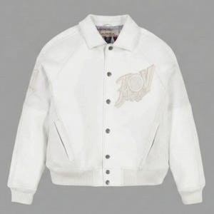 May include: A white varsity-style jacket featuring a classic collar, snap-button front closure, and ribbed cuffs and hem. The jacket includes a large embroidered patch on the left chest and textured side panels, with the Avirex brand label visible at the neck.