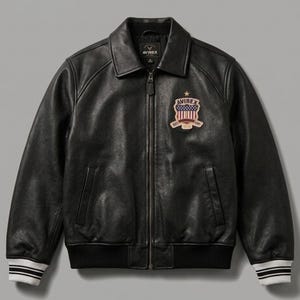 May include: A black leather jacket with a front zipper closure, a pointed collar, and ribbed cuffs featuring white stripes. A patch on the left chest displays the text AVIREX, a star, and a shield graphic with red and white vertical stripes.