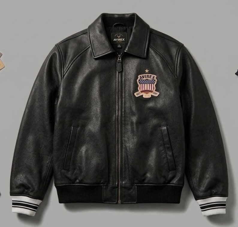 May include: A black leather jacket with a front zipper closure, a pointed collar, and ribbed cuffs featuring white stripes. A patch on the left chest displays the text AVIREX, a star, and a shield graphic with red and white vertical stripes.