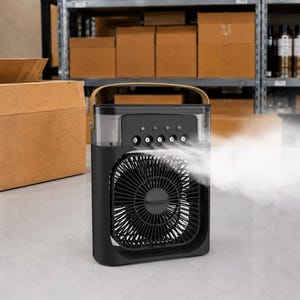 Puede incluir: Enfriador de aire port&aacute;til negro y gris con un asa marr&oacute;n. La parte delantera presenta un ventilador con un dise&ntilde;o circular. La parte superior tiene botones de control. Se emite niebla visible desde la parte delantera del enfriador. El fondo muestra estantes con cajas de cart&oacute;n.