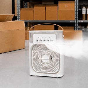 Puede incluir: Un enfriador de aire port&aacute;til blanco con un asa marr&oacute;n. La parte delantera presenta un ventilador con un dise&ntilde;o circular. El panel de control tiene varios botones e indicadores luminosos. Es visible una corriente de aire fresco, lo que sugiere que el dispositivo est&aacute; en funcionamiento.