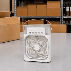 Puede incluir: Un enfriador de aire port&aacute;til blanco con un asa marr&oacute;n. El dispositivo tiene un ventilador cuadrado y botones de control. El fondo incluye cajas de cart&oacute;n en estanter&iacute;as.