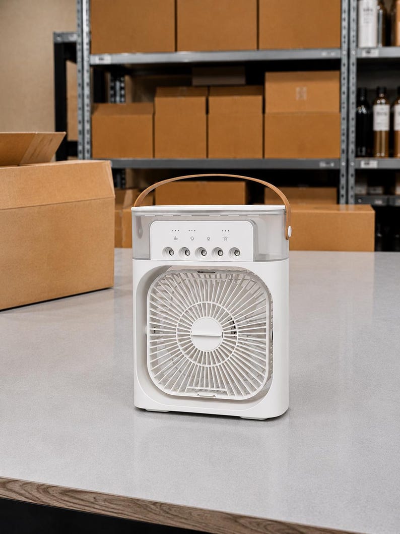 Puede incluir: Un enfriador de aire port&aacute;til blanco con un asa marr&oacute;n. El dispositivo tiene un ventilador cuadrado y botones de control. El fondo incluye cajas de cart&oacute;n en estanter&iacute;as.