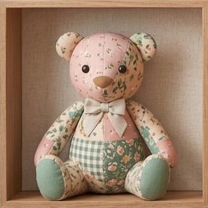 Pode incluir: Um urso de peluche feito de vários retalhos de tecido com padrões florais em tons de rosa, verde e creme. O urso tem olhos redondos escuros, um nariz castanho e um laço de cor creme à volta do pescoço.
