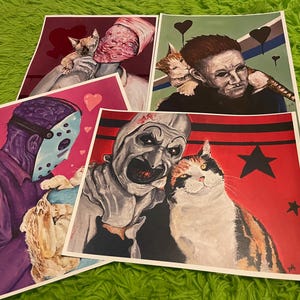May include: Four different art prints featuring horror movie characters with cats. Each print has a different color scheme and features a different character. The prints are all in a square format.