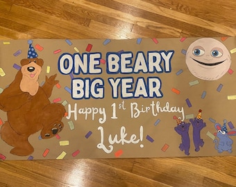 May include: A tan rectangular banner featuring a brown bear in a blue party hat, a smiling moon, and two small purple creatures. The text reads ONE BEARY BIG YEAR, Happy 1st Birthday, and Luke, surrounded by colorful confetti illustrations.