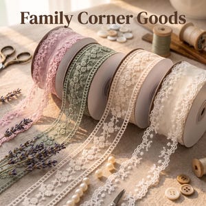 Op de afbeelding: Vier rollen decoratief kanten lint in roze, saliegroen, crème en wit, elk met ingewikkeld bloemenborduurwerk en geschulpte randen. De tekst Family Corner Goods staat bovenaan. Inclusief lavendeltakjes en knopen.