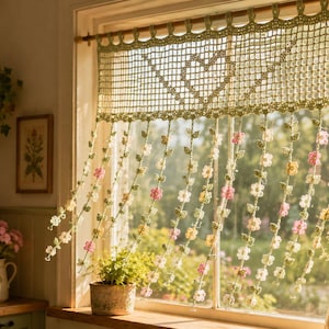 May include: A sage green crochet valance curtain featuring a central heart motif in a grid pattern. The bottom edge consists of multiple hanging strands decorated with small, multi-coloured crocheted flowers in shades of pink, yellow, and white.