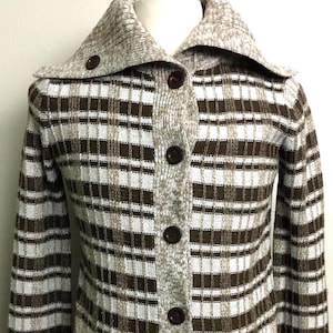 May include: A long-sleeved knit cardigan featuring a brown and white plaid pattern, a large fold-over collar, and a front button closure with dark brown buttons. The garment includes two front pockets and ribbed cuffs on the sleeves.