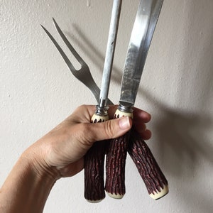 May include: A set of three kitchen knives with faux antler handles. The knives include a carving knife, a steak knife, and a fork.