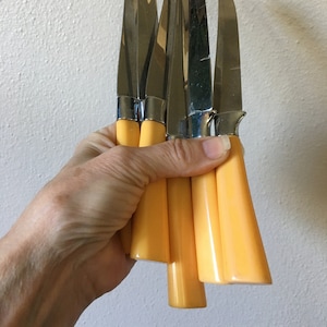 May include: A set of six yellow handled butter knives with silver blades.