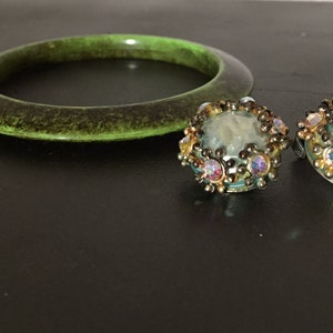 May include: A set of green plastic bangle bracelet and a pair of iridescent glass earrings with a gold tone metal setting.