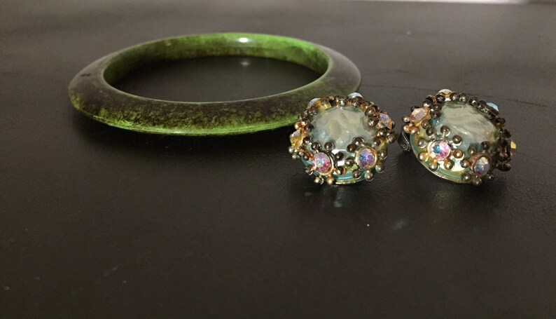 May include: A set of green plastic bangle bracelet and a pair of iridescent glass earrings with a gold tone metal setting.