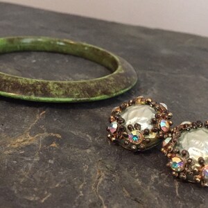 May include: A green bangle bracelet with a brown marbled pattern and a pair of round earrings with iridescent rhinestones and a pearl-like center.