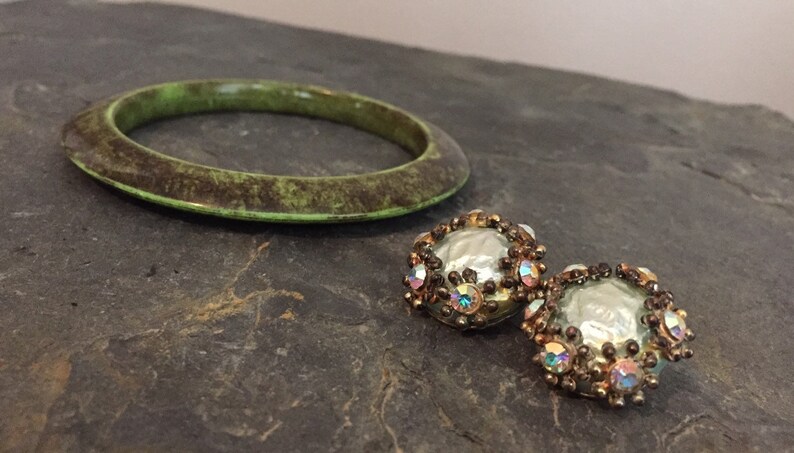 May include: A green bangle bracelet with a brown marbled pattern and a pair of round earrings with iridescent rhinestones and a pearl-like center.