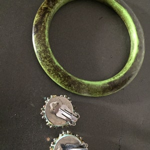 May include: A pair of green and blue beaded clip-on earrings with silver clasps. The earrings are next to a green bangle bracelet with a dark brown speckled pattern.
