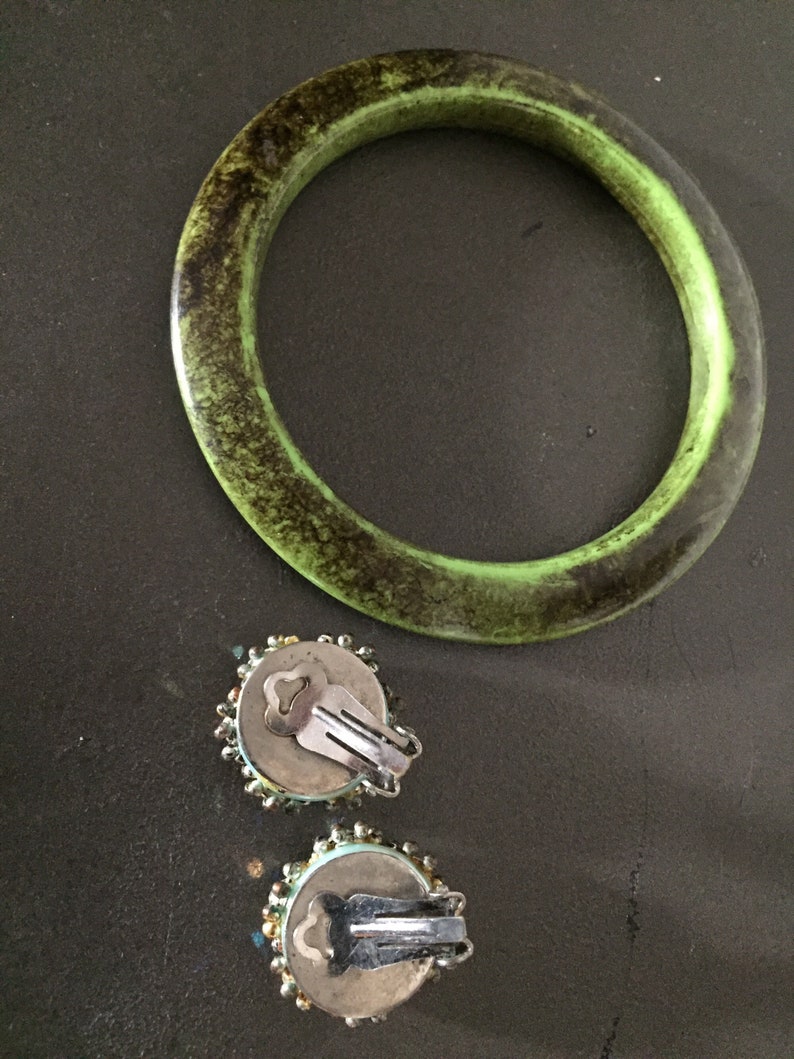 May include: A pair of green and blue beaded clip-on earrings with silver clasps. The earrings are next to a green bangle bracelet with a dark brown speckled pattern.