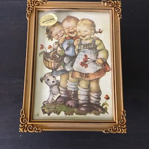 May include: A vintage wooden music box with a gold frame and a picture of three children laughing. The picture is by artist,  "Hummel". The music box has a label that reads "Hummel - Made in Germany".