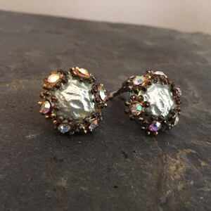 May include: A pair of silver and gold tone earrings with iridescent rhinestones. The earrings feature a round, textured center piece.