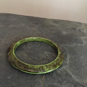 May include: A green and brown bangle bracelet with a mottled pattern. The bracelet is made of a smooth, hard material.