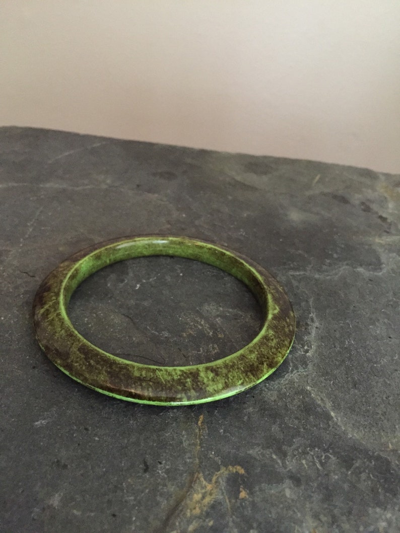 May include: A green and brown bangle bracelet with a mottled pattern. The bracelet is made of a smooth, hard material.