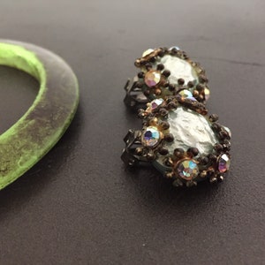 May include: A pair of silver tone earrings with iridescent rhinestones and a light blue center. The earrings are on a dark gray surface.