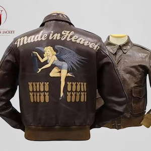 May include: Two brown leather jackets are displayed. One jacket features a design on the back with the text "Made in Heaven" and an illustration of a woman with angel wings. The other jacket is a solid brown color.