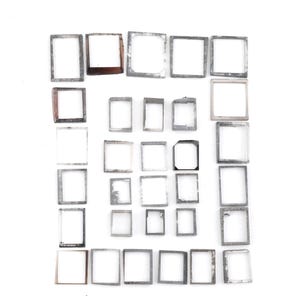 May include: A collection of twenty-eight rectangular metal frames arranged in a grid pattern. The frames vary in size and thickness, featuring metallic silver, grey, and copper-toned finishes with some showing signs of wear and oxidation.