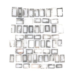 Peut inclure: Une collection de nombreux petits cadres rectangulaires disposés en grille. Chaque cadre présente une finition texturée, grise, semblable à de la pierre, avec des degrés d'usure variés et des bords irréguliers, entourant un espace central vide.