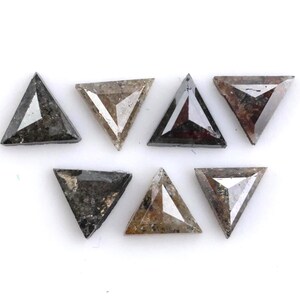 May include: Seven loose triangular-cut diamonds arranged in two rows. The stones feature varied textures and colors, ranging from dark charcoal gray and metallic black to translucent light brown and speckled earth tones with faceted surfaces.