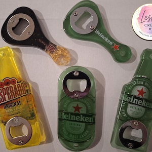 Pu&ograve; includere: Una collezione di apribottiglie di varie forme e colori. Ci sono due apribottiglie Heineken verdi, uno a forma di bottiglia. Sono presenti anche un apribottiglie Desperados giallo e un apribottiglie nero con manico dorato.