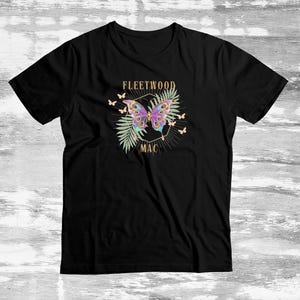 May include: Black t-shirt with a vibrant butterfly design and the words "FLEETWOOD MAC". The butterfly is decorated with purple, blue, and yellow, set against green leaves and small butterflies.