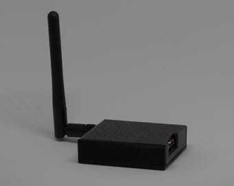 Könnte beinhalten: Ein schwarzer, rechteckiger drahtloser Netzwerkadapter mit einer einzelnen vertikalen Antenne an der Seite. Das Gerät hat eine texturierte, matte Oberfläche und einen sichtbaren Micro-USB-Anschluss an der Seitenwand für die Datenübertragung.