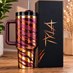 May include: A maroon and gold insulated tumbler with a handle and a straw. The tumbler has a decorative pattern and is next to a black box with copper-colored text. The tumbler is designed to keep drinks cold or hot.