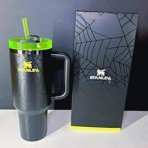 May include: A black Stanley tumbler with a spiderweb pattern, a neon green lid, and a matching neon green straw, accompanied by a tall black rectangular box featuring a matching spiderweb design and the white Stanley logo on the front.