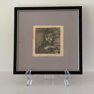 May include: A framed black and white etching on paper featuring a portrait with expressive lines. The artwork is titled "Prophet" and signed "George Tilyer" in pencil. It is housed in a black frame with a gray mat and a thin silver inner border.