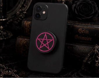 May include: A black smartphone featuring a circular phone grip attached to the back. The grip is black with a vibrant pink pentagram symbol printed in the centre, consisting of a five-pointed star enclosed within a circular border.